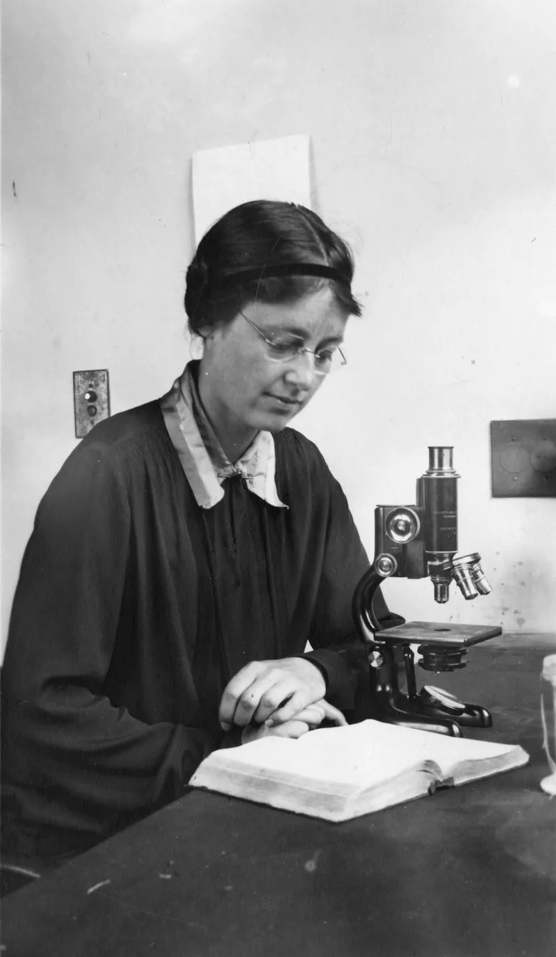 scientist Drew-Baker reads a book by her microscope