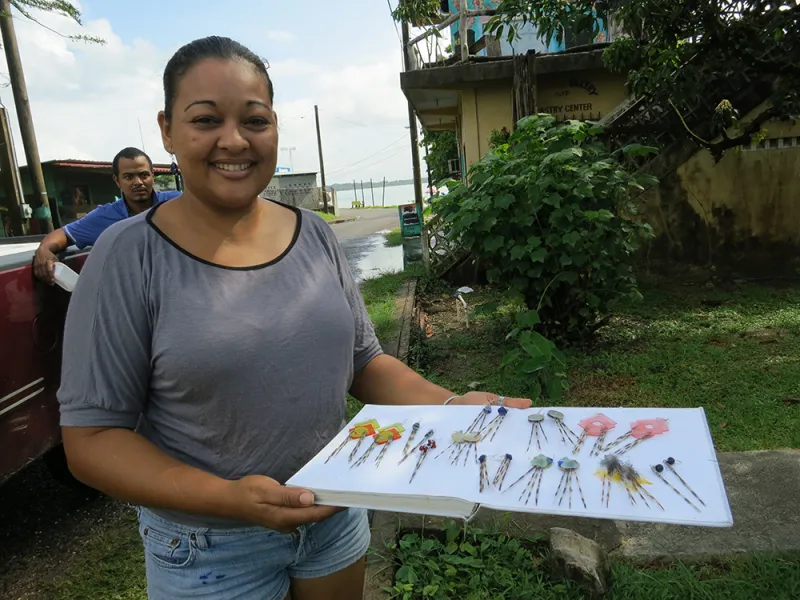 A woman stands holding a white tray that displays lionfish jewelry.