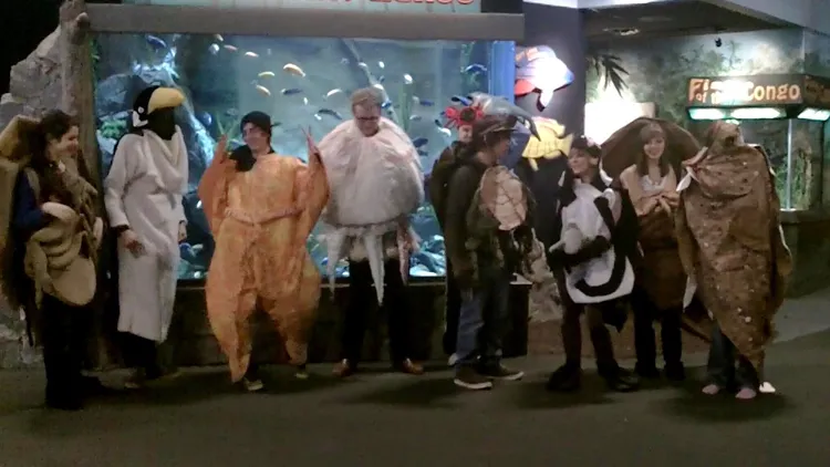 Students in marine life costumes pose in an aquarium.
