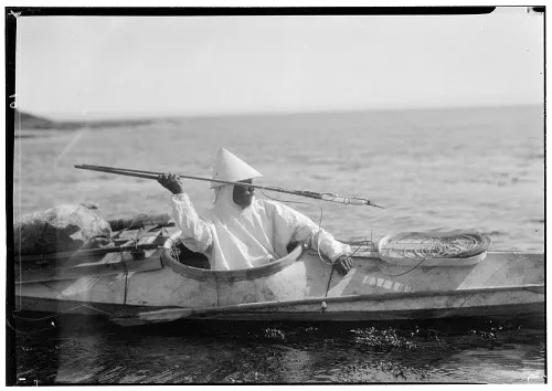 a hunter throws a harpoon from the cockpit of his kayak