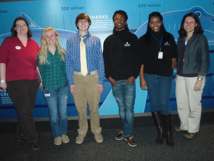 Students studying climate change pose for a photo against a wall.