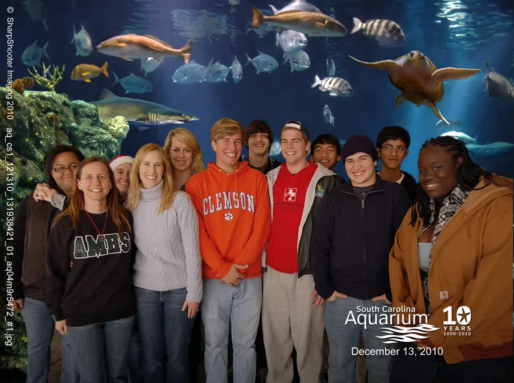 Students pose in front of an aquarium tank with fish.