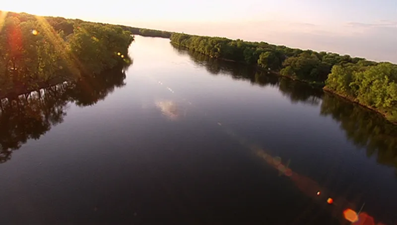 An aerial shot of a tree-lined section of the Mississippi River at sunset.
