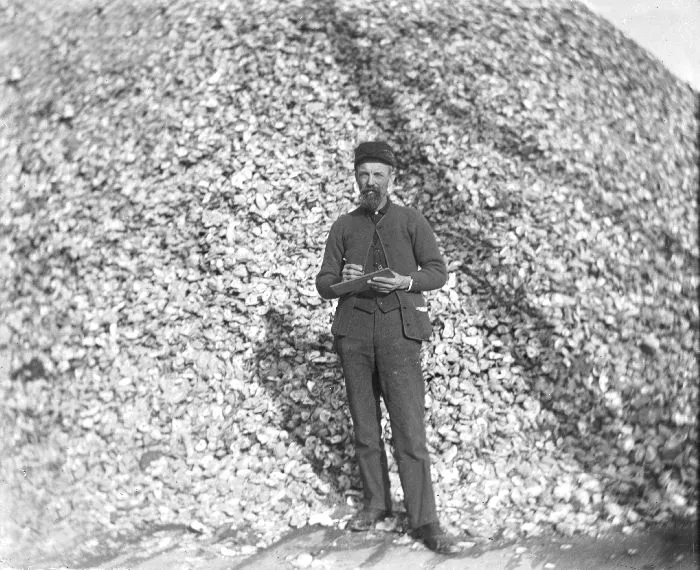 A longshoreman standing in front of a large pile of oyster shells on waterfront pier in Atlantic City in 1910.