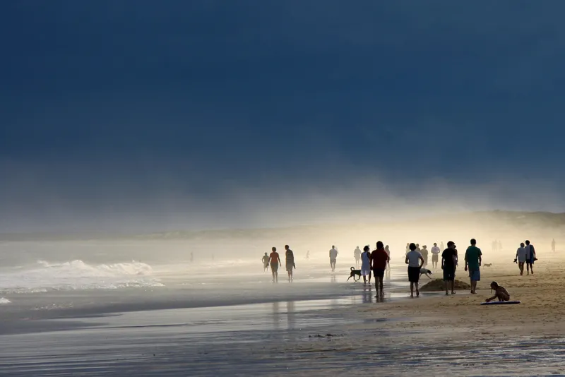 A beach scene with groups of people walking in the water and playing with the sand.