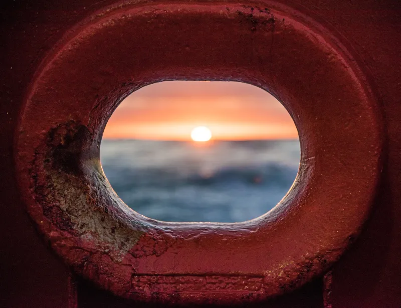 an ocean sunrise through a red metal hole