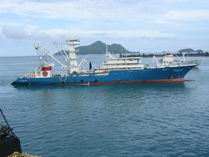 A large blue and red fishing vessel sits on the water. 