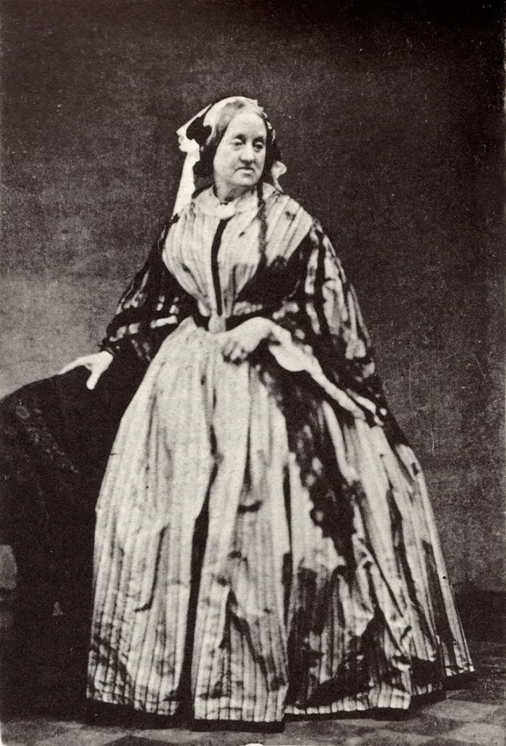 a Victorian woman poses in a full length dress