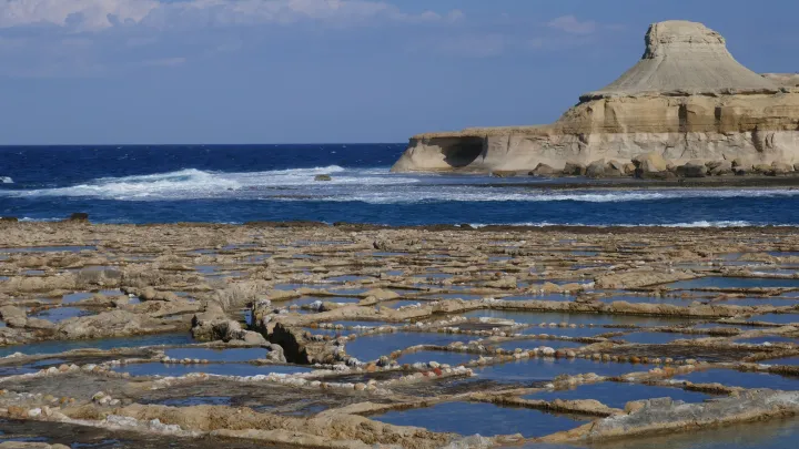 shallow pans carved out of the sea coast create many pools with a seascape in the background