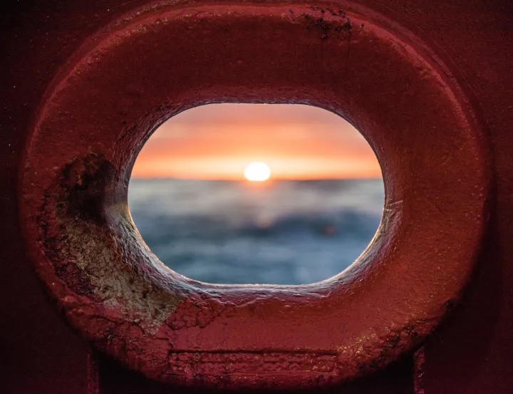 an ocean sunrise through a red metal hole