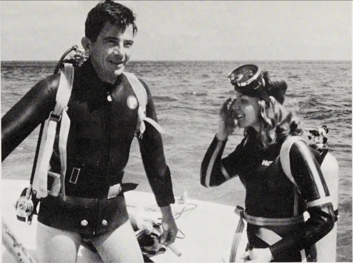 a man and a women in scuba gear on the deck of a ship