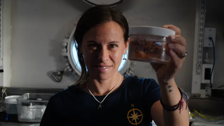 a female scientist in a blue shirt holds up a jar