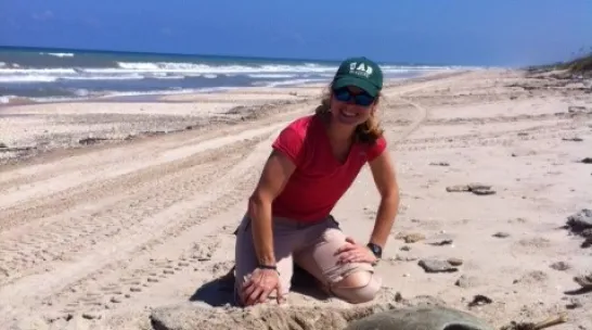 Elizabeth Bevan sitting on the beach with a sea turtle.