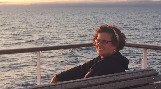 Karen Romano Young sitting on a bench with a sunset in the background.