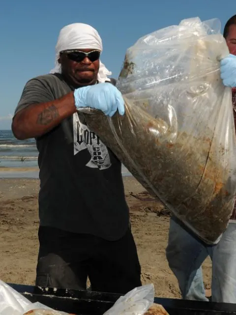 Two men carry a large bag of oily waste