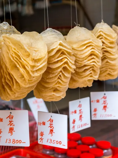 Dried light brown swim bladders hang from a string at a market.