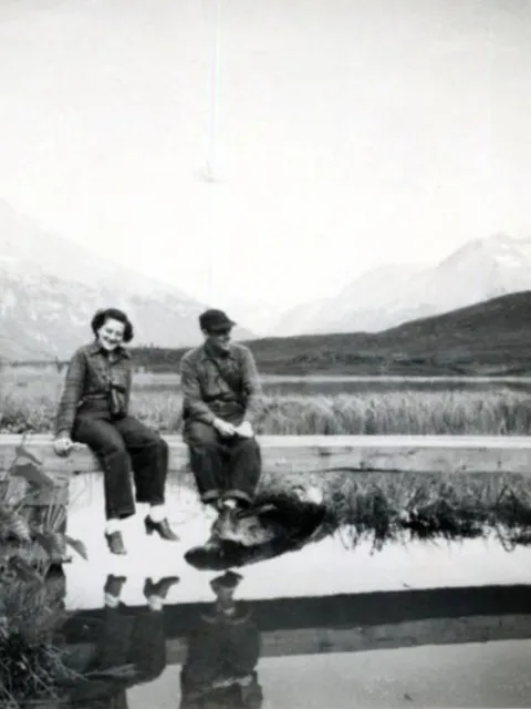 a man and a woman sitting on a pier amid mountains
